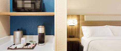 Habitación de hotel con microondas en un estante, cafetera y un cubo de basura.