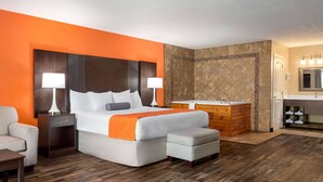 A hotel room with a large bed, a wooden dresser, a vanity with a mirror, and a bathtub. - Howard Johnson by Wyndham Pigeon Forge (Pigeon Forge)