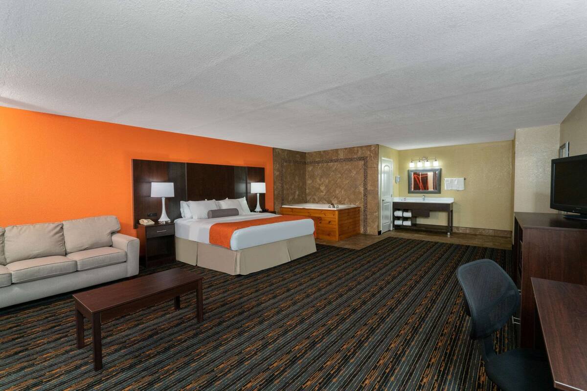 Una camera d'albergo con un letto, una scrivania, una televisione, un divano e un bagno con vasca e doccia.