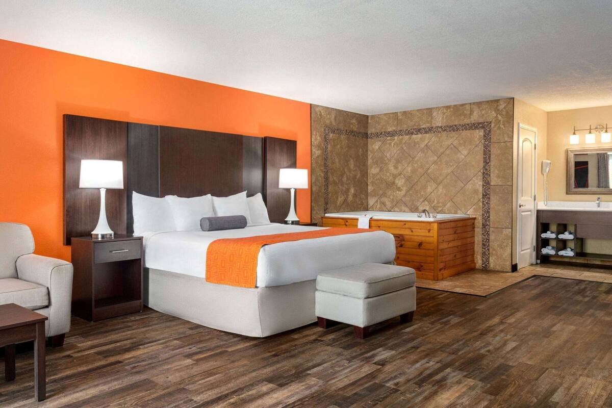 Una camera d'albergo con un letto, comodini, una sedia, una scrivania, un angolo trucco con specchio, una vasca e uno spazio doccia.