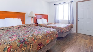 A hotel room with two beds, a wooden headboard, a nightstand with a lamp, a window with curtains, and a door. - Country Hearth Inn & Suites By OYO Sturgis (Sturgis)