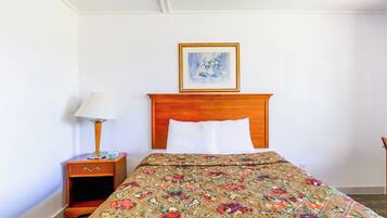 A hotel room with a wooden headboard, a floral bedspread, a nightstand with a lamp, and a framed picture on the wall.
