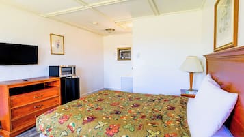 Habitación de hotel con cama, cómoda de madera, televisor de pantalla plana, microondas, lámpara y un cuadro en la pared.