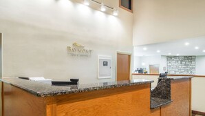 A reception desk with a wooden finish and granite top, a sign above it reading "Baymont Inn & Suites," and a stone wall in the background. - Baymont by Wyndham Metropolis (Metropolis)