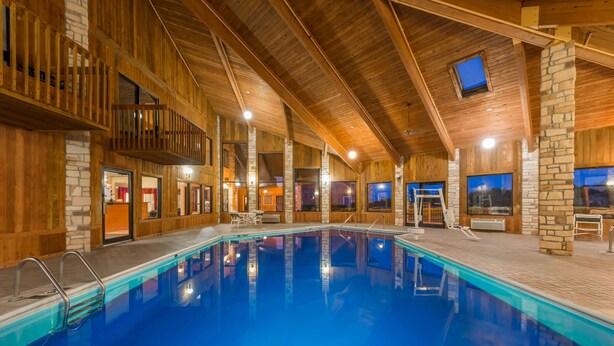 An indoor swimming pool with wooden walls and stone accents, surrounded by seating areas and a balcony. - Baymont by Wyndham Metropolis (Metropolis)