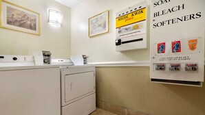 A laundry area with a washing machine, a coin-operated dryer, and a wall-mounted dispenser for soap, bleach, and softeners. - Super 8 by Wyndham Charlotte University (Charlotte)