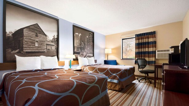 A hotel room with two beds, a desk, a chair, a TV, and large framed pictures on the wall. - Super 8 by Wyndham Charlotte University (Charlotte)