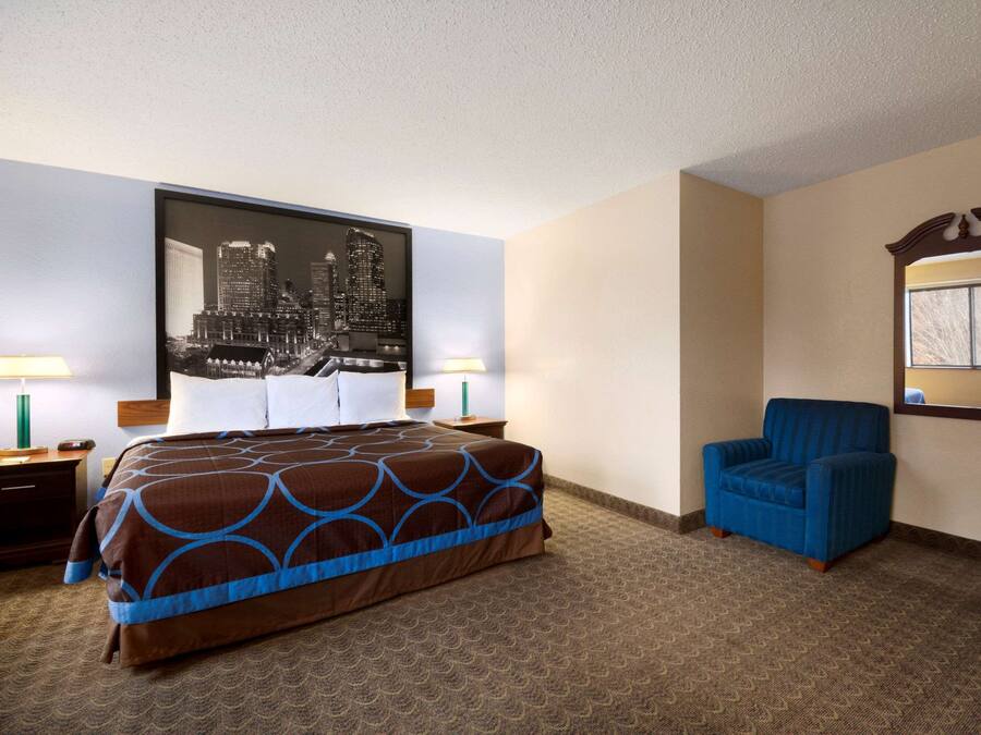 Ein Hotelzimmer mit einem großen Bett, zwei blauen Sesseln, einem Stadtbild, einem Spiegel und einem Fenster mit Vorhängen.