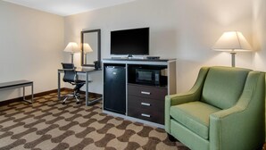 Ein Hotelzimmer mit Schreibtisch, Stuhl, Fernseher, Mikrowelle und einem grünen Sessel.