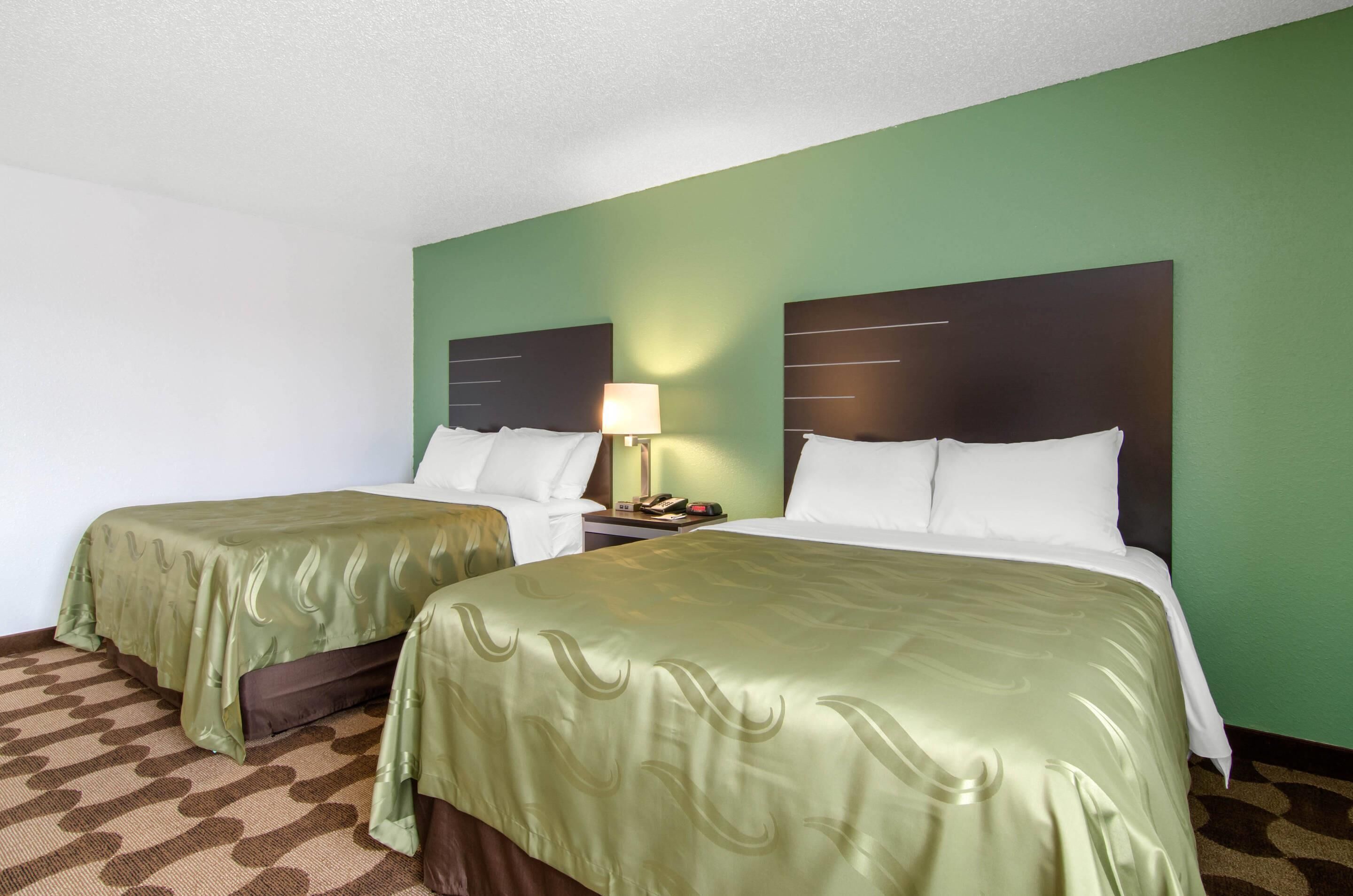A hotel room with two beds, green walls, and a patterned carpet.