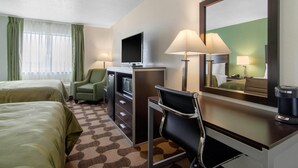 Ein Hotelzimmer mit zwei Betten, einem Schreibtisch mit Computer, einem Stuhl, einem Fernseher und einer Kaffeemaschine.