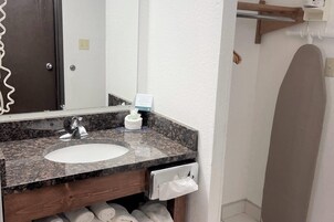 Un baño con lavamanos de encimera de granito, un espejo, un perchero y un mueble de madera debajo del lavabo.