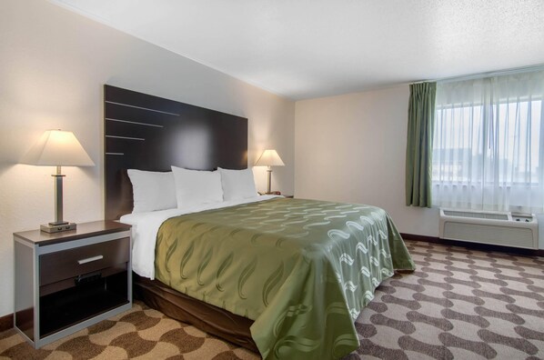 A hotel room with a bed, two bedside tables with lamps, a window with curtains, and an air conditioning unit.