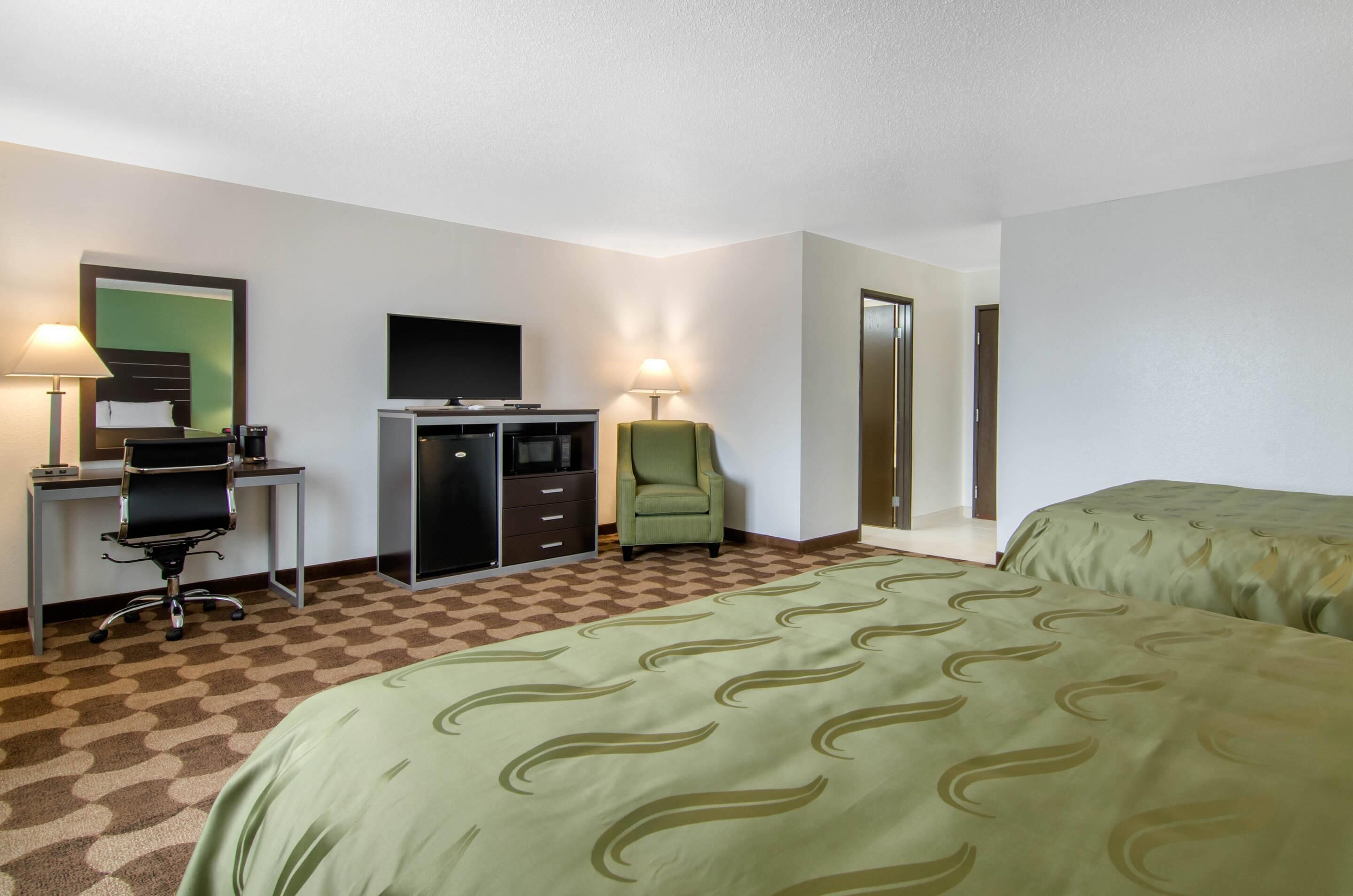 A hotel room with a bed, desk, chair, TV, and wardrobe.