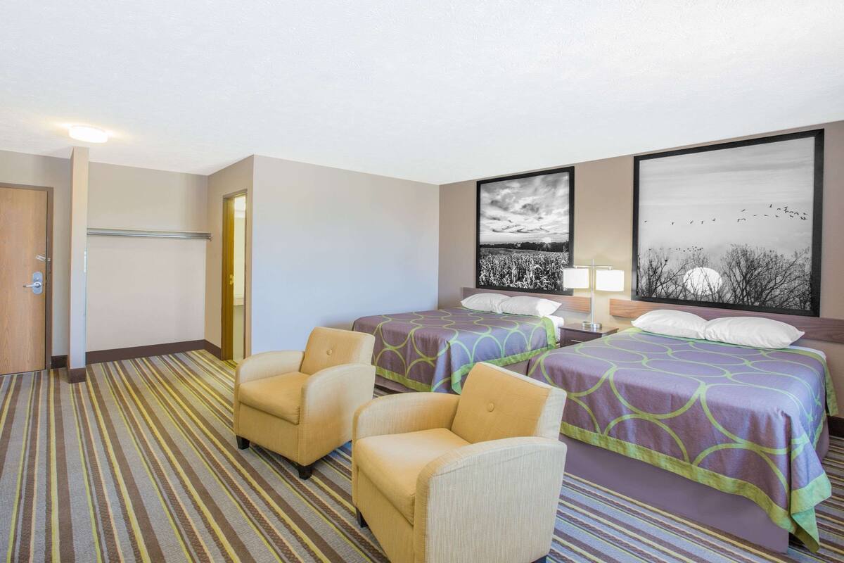 Une chambre d’hôtel avec deux lits, un coin salon avec des fauteuils, une porte et deux œuvres d’art mural.