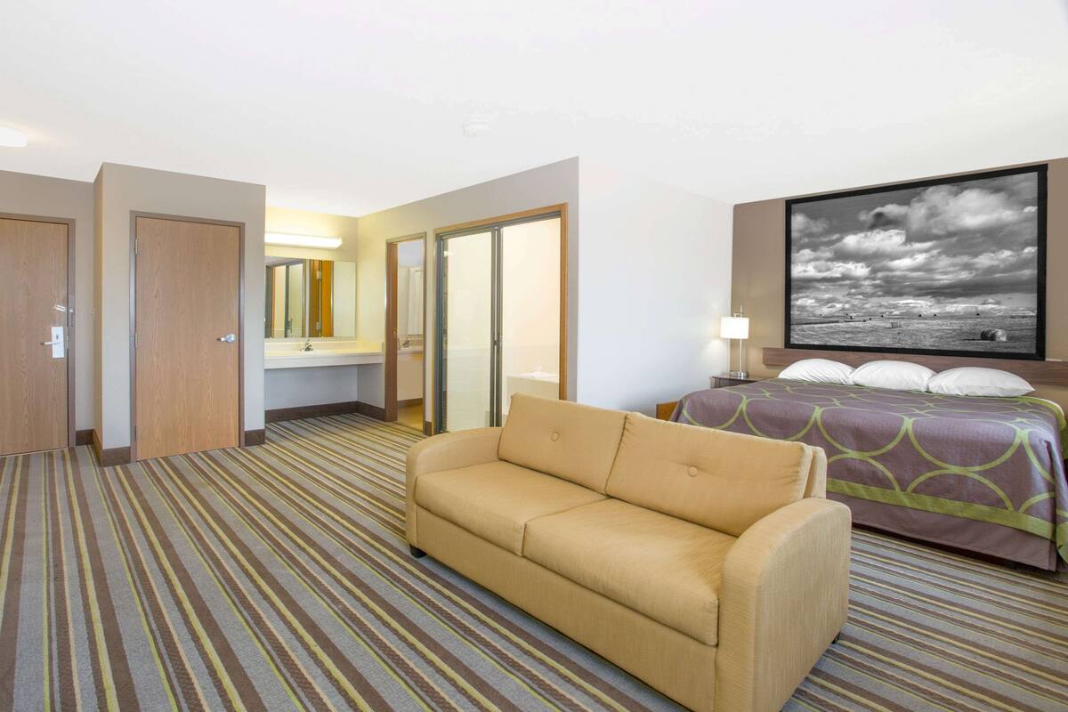 Une chambre d’hôtel avec un canapé, un lit recouvert d’une couvre-lit à motifs, un grand tableau encadré au mur et un tapis rayé.