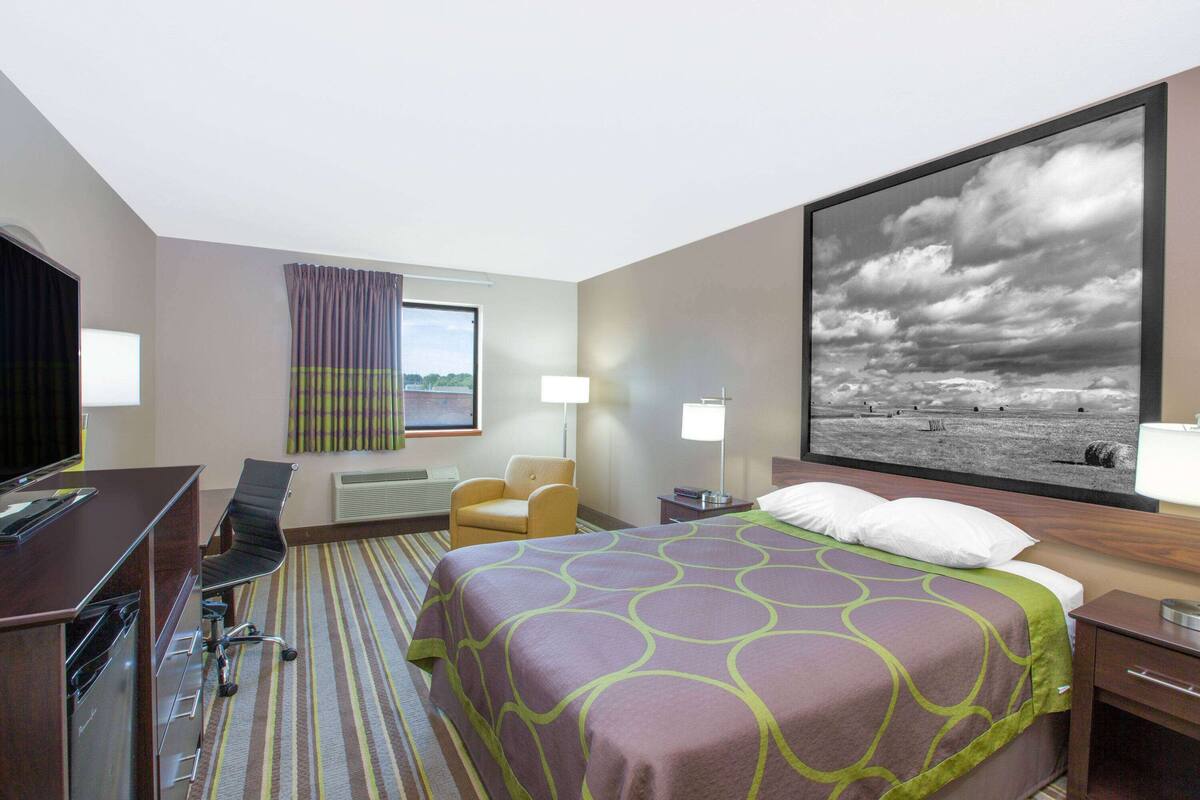 Une chambre d’hôtel avec un lit, un bureau, une chaise, une télévision et une grande fenêtre avec des rideaux.