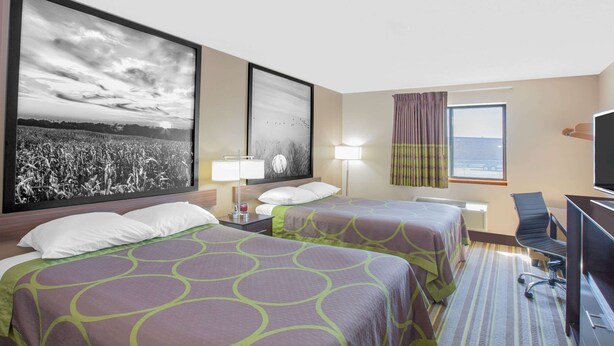 A hotel room with two beds, a desk, a chair, a television, and large framed pictures on the wall.