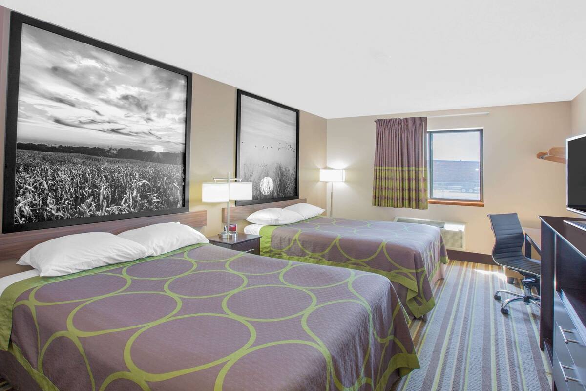 Une chambre d’hôtel avec deux lits, un bureau, une chaise, une télévision et de grandes images encadrées accrochées au mur.