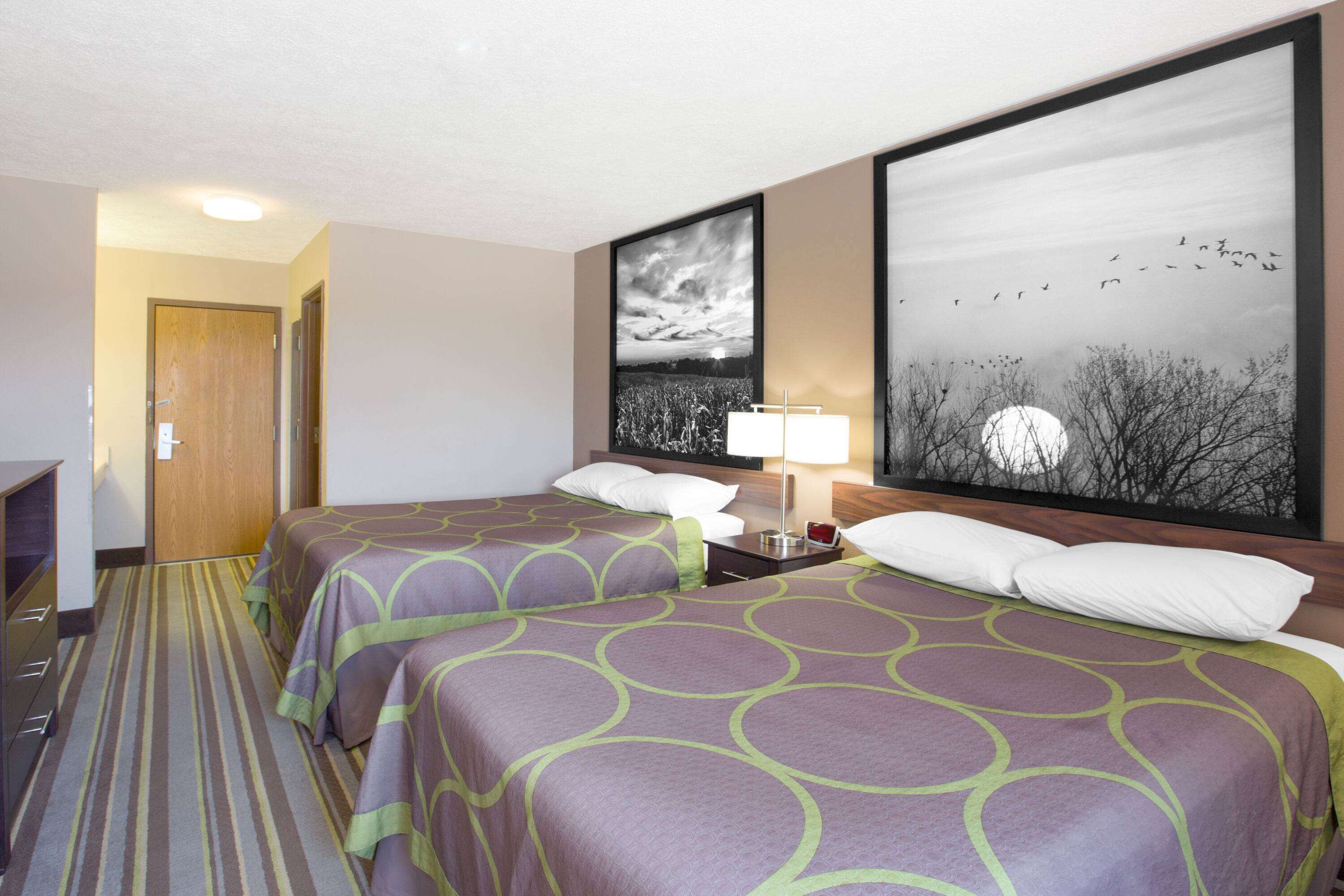 A hotel room with two beds, a nightstand with a lamp, and two framed pictures on the wall.