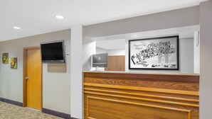 A reception area with a wooden reception desk, a flat-screen TV mounted on the wall, and a framed welcome sign.