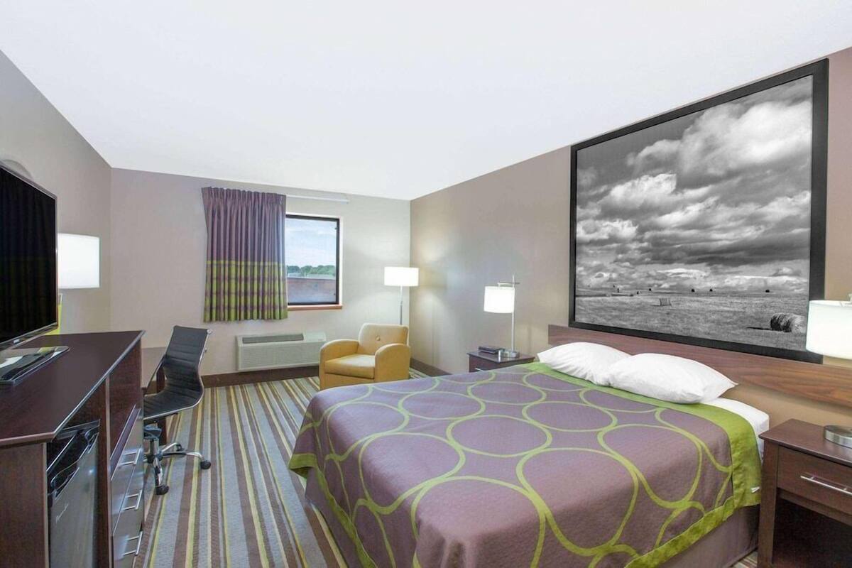 Une chambre d’hôtel avec un lit, un bureau, une chaise et une grande fenêtre.
