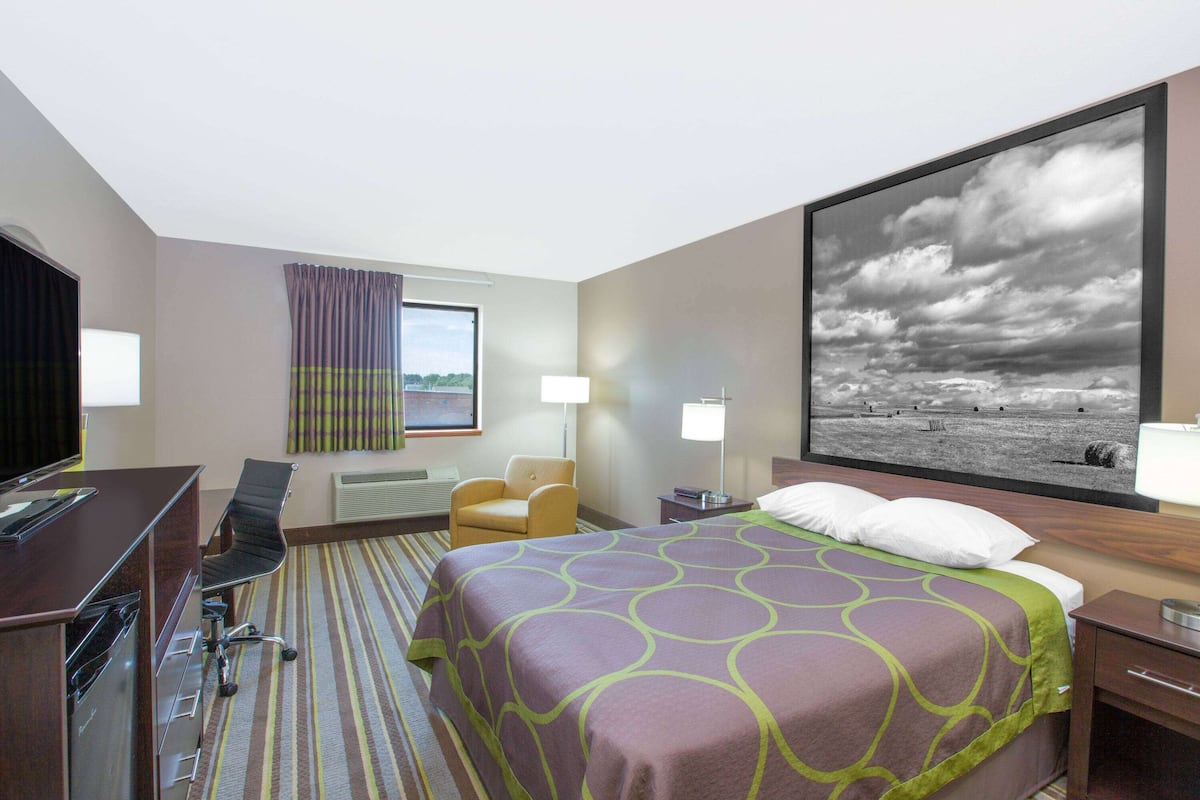 Une chambre d’hôtel avec un lit, un bureau, une chaise et un grand tableau représentant une scène de plage.