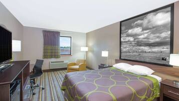 A hotel room with a bed, desk, chair, and a large painting of a beach scene.