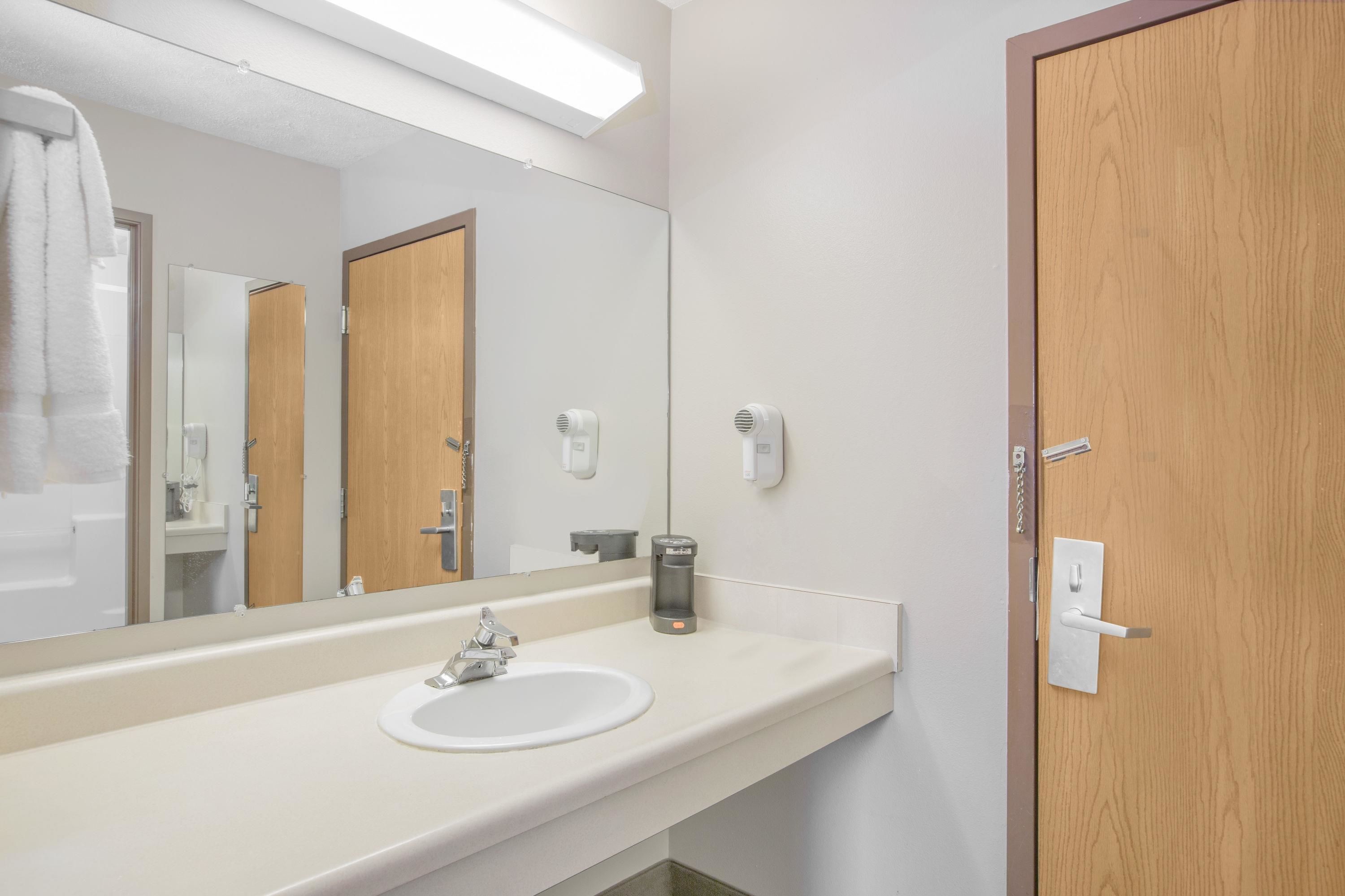 A bathroom with a white sink, a mirror, a towel rack, and a wooden door.