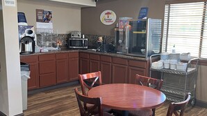 A breakfast area with a round wooden table and chairs, a microwave, a coffee machine, and a refrigerator.