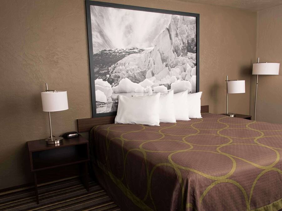 A hotel room with a large bed, two bedside lamps, a nightstand with a lamp, and a framed photograph on the wall.