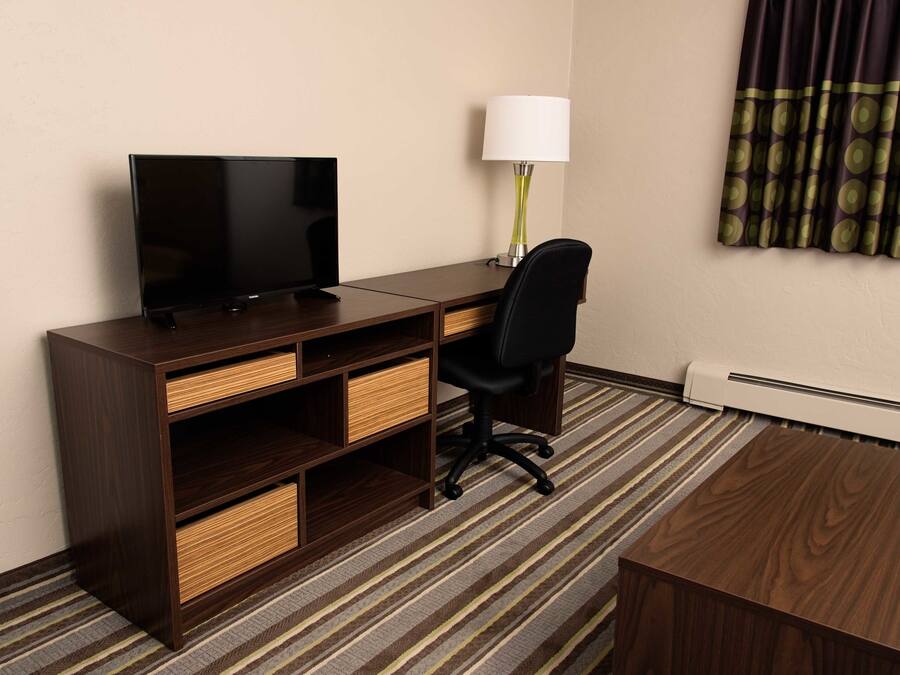 A hotel room with a wooden desk, a television, a lamp, a chair, and a carpeted floor.