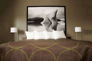 Una habitación de hotel con una cama grande, dos lámparas de noche y una fotografía enmarcada de un iceberg en la pared.