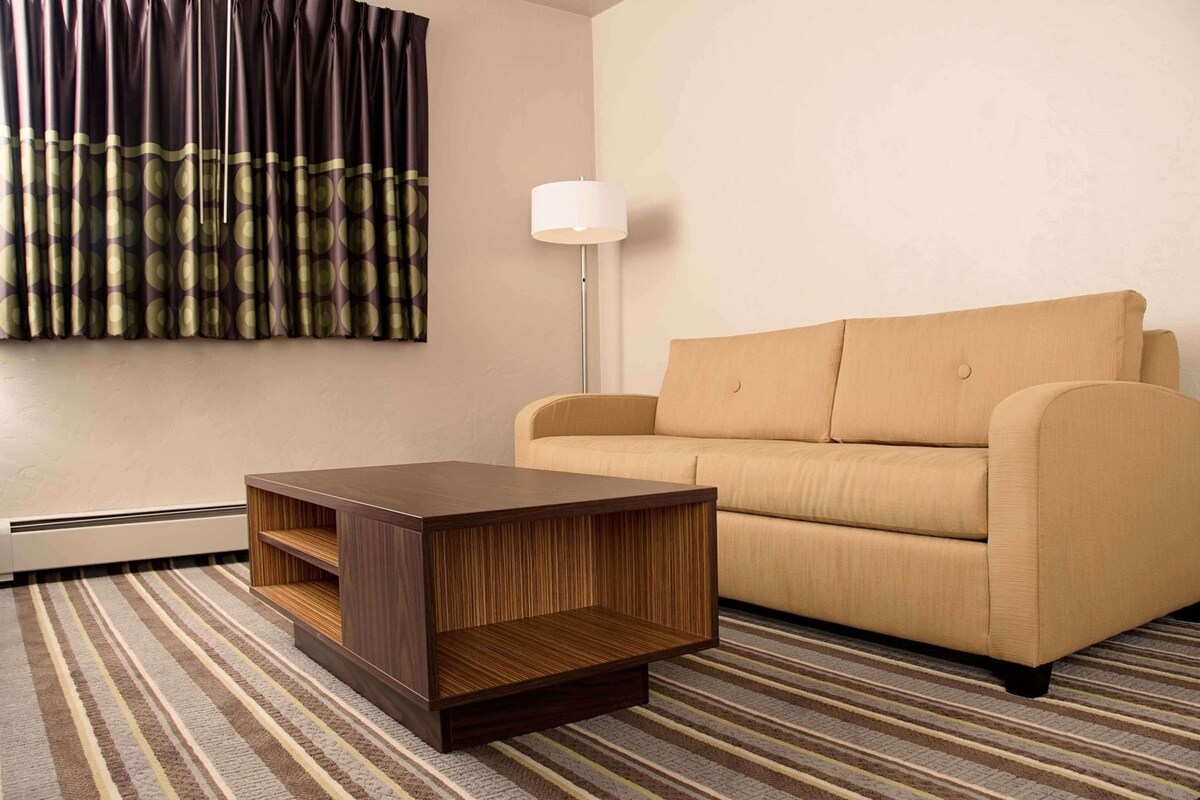A living room with a sofa, a coffee table, a floor lamp, and a wall-mounted artwork.