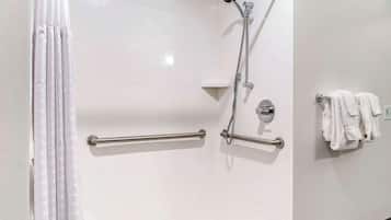 Un baño moderno con ducha, barras de apoyo, toallero y pared revestida de azulejos blancos.