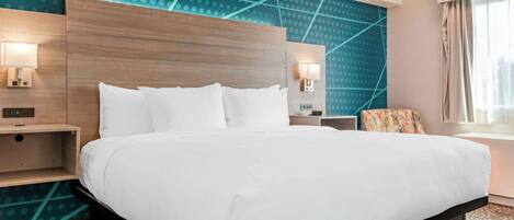 Habitación de hotel con una cama grande, cabecera de madera, dos mesitas de noche con lámparas, un papel tapiz decorativo y una ventana con cortinas.