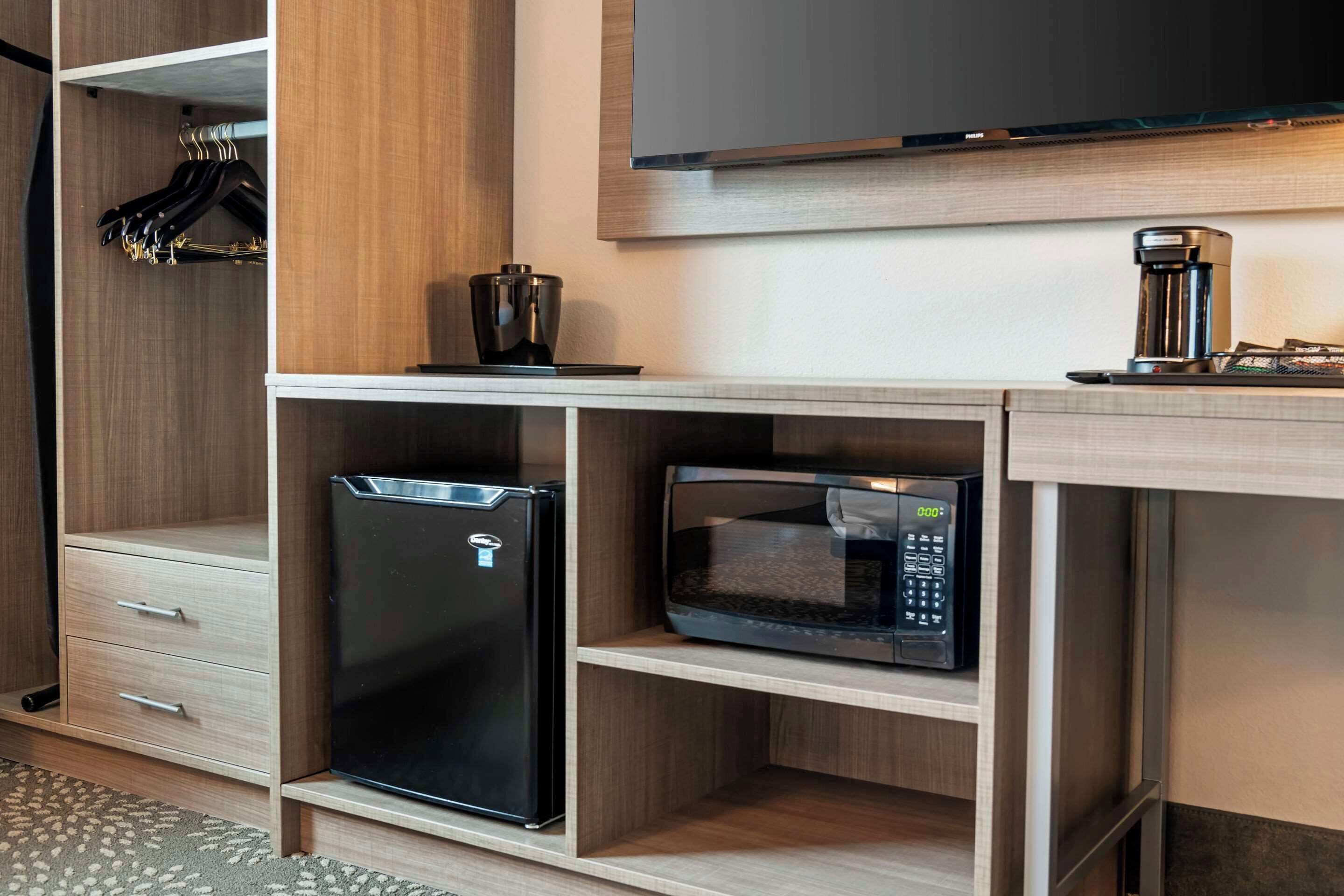 A compact kitchenette with a refrigerator, microwave, and coffee maker on a wooden countertop.