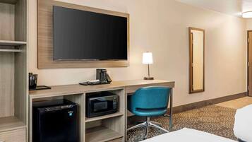 Habitación de hotel con televisión de pantalla plana, escritorio con cafetera, microondas, una silla azul y una cama.