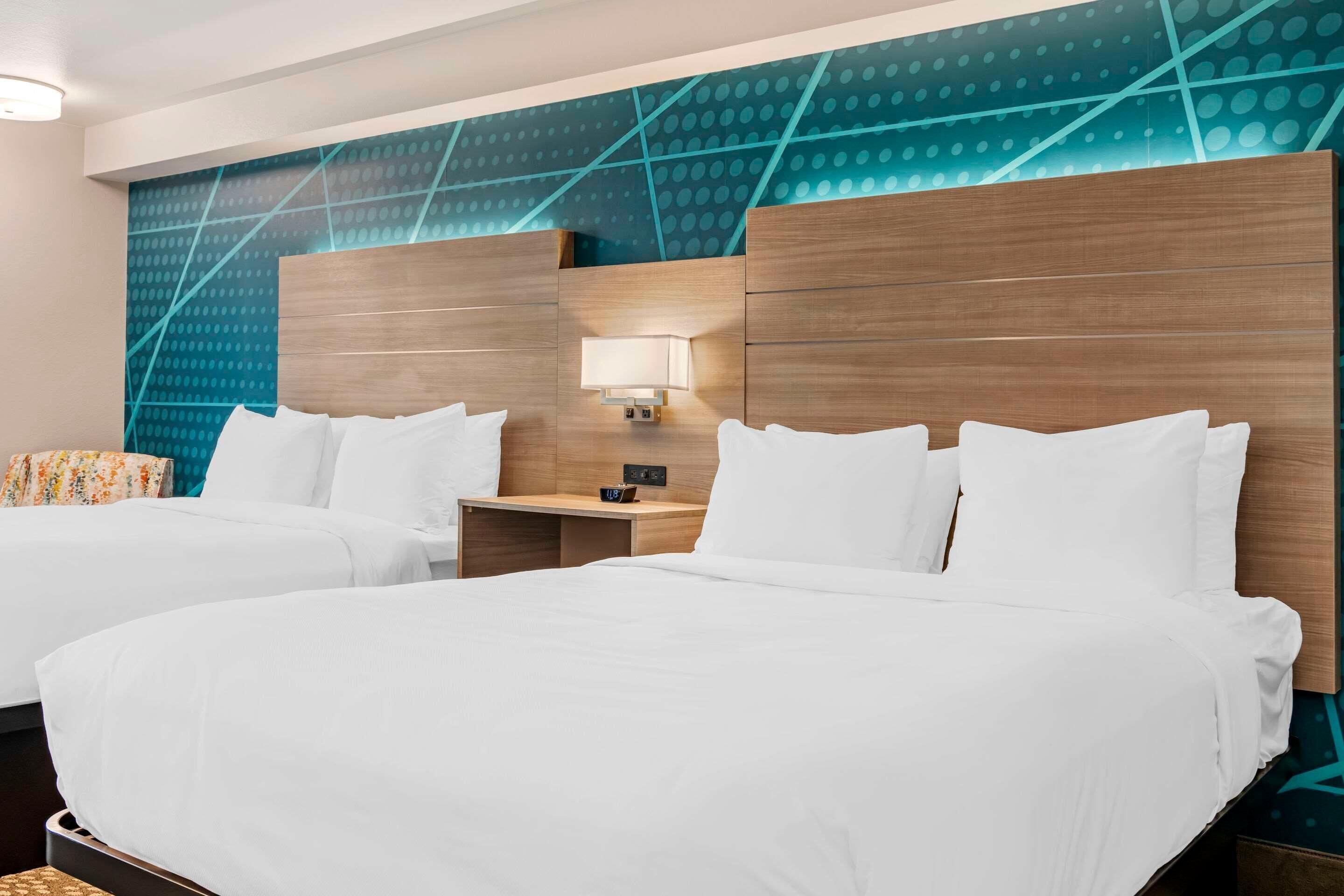 A hotel room with two beds, a nightstand with a lamp, and a wall with a geometric pattern.