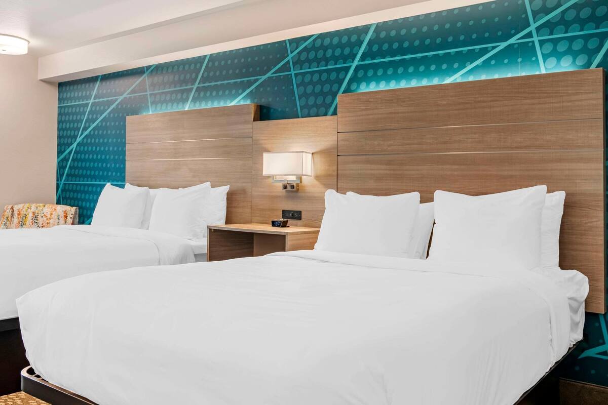 A hotel room with two beds, a nightstand with a lamp, and a wall with a geometric pattern.