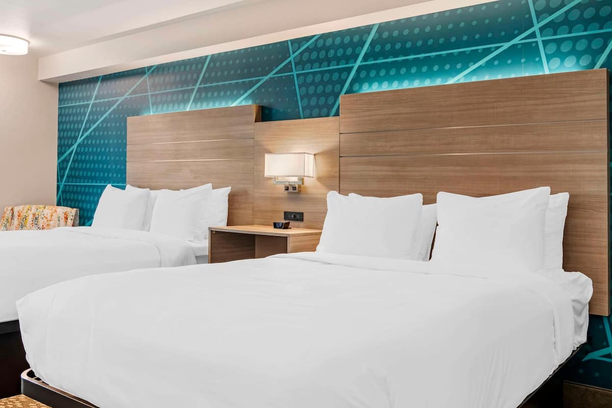 A hotel room with two beds, a nightstand with a lamp, and a wall with a geometric pattern.