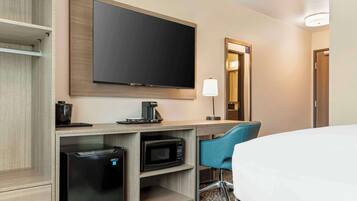 Habitación de hotel con cama, escritorio con computadora, microondas, cafetera, televisor y una silla.