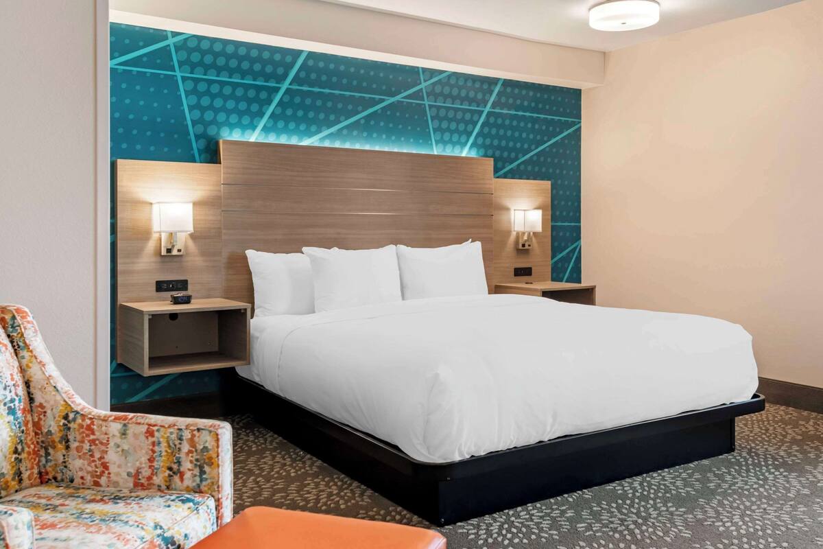 A hotel room with a large bed, two bedside tables with lamps, a colorful chair, and a patterned carpet.