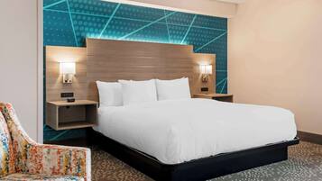 A hotel room with a large bed, two bedside tables with lamps, a colorful chair, and a patterned carpet.