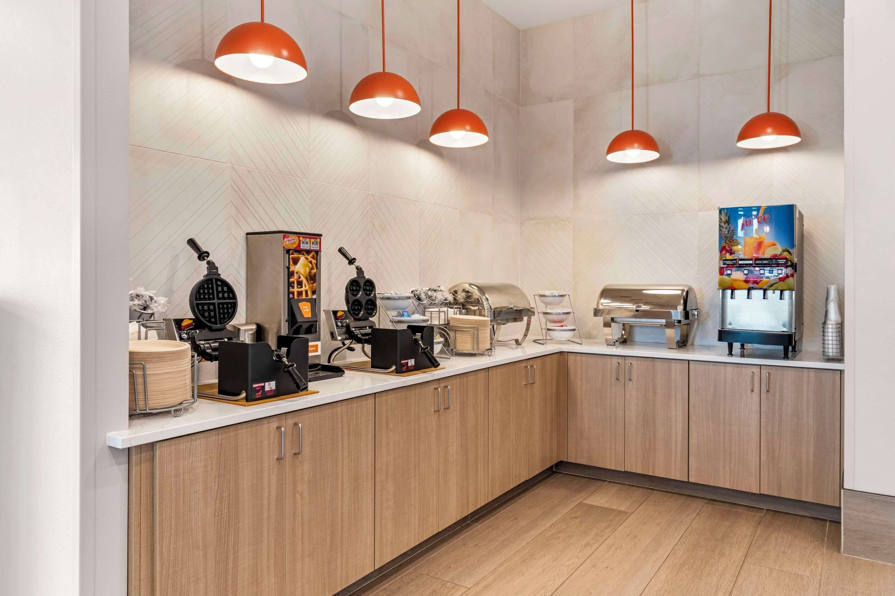 Una cocina moderna con encimera blanca, armarios de madera y lámparas colgantes rojas.