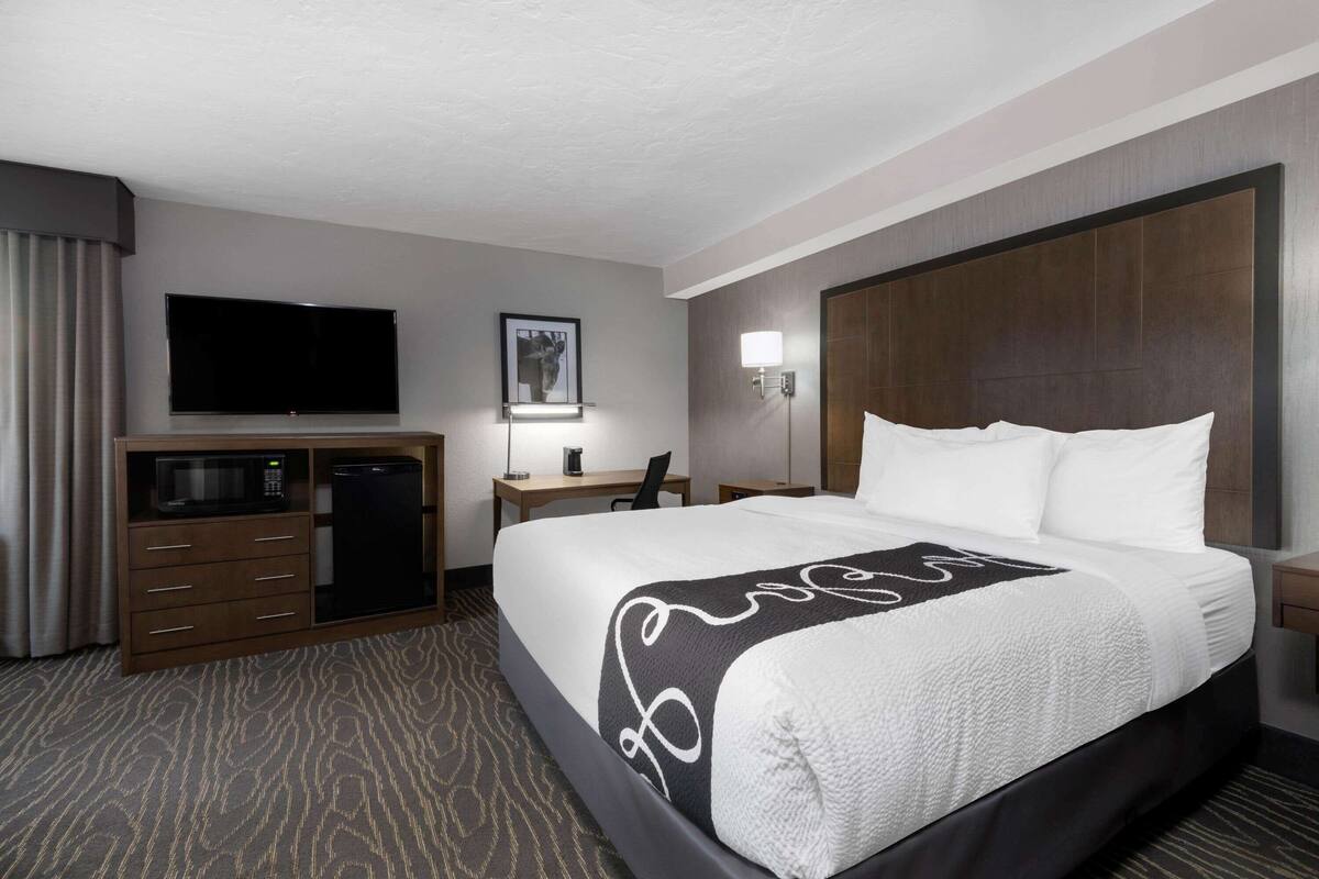 Habitación de hotel con cama, escritorio con computadora, televisor y minibar.