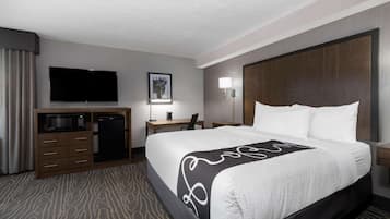 A hotel room with a bed, a desk with a computer, a television, and a minibar.