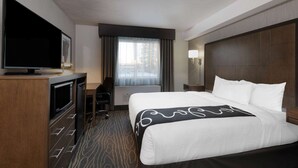 A hotel room with a bed, a desk with a television, a chair, and a window with curtains.