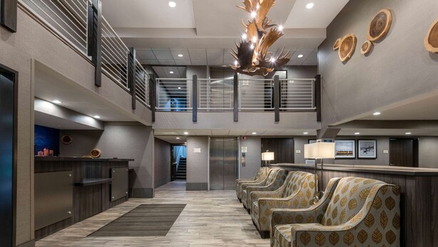 A hotel lobby with a reception desk, a staircase, and a seating area with patterned chairs.