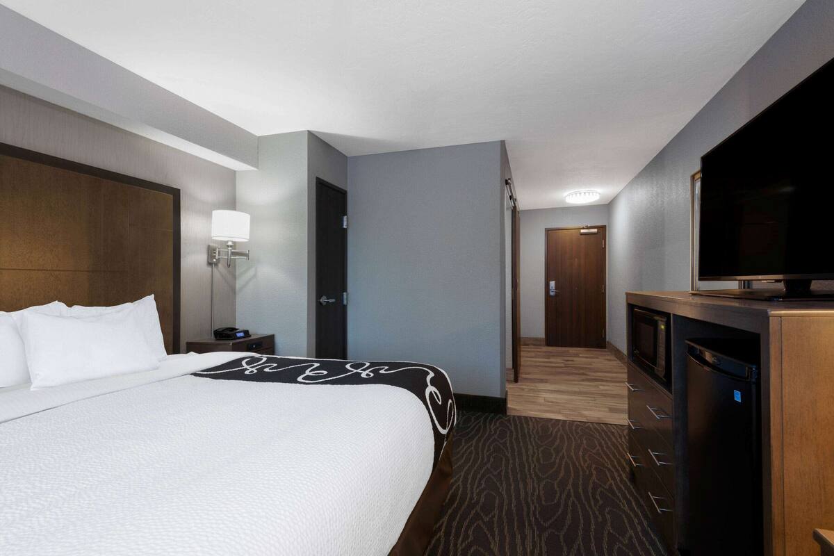 Una habitación de hotel con una cama grande, televisión de pantalla plana, microondas y un escritorio pequeño con lámpara.